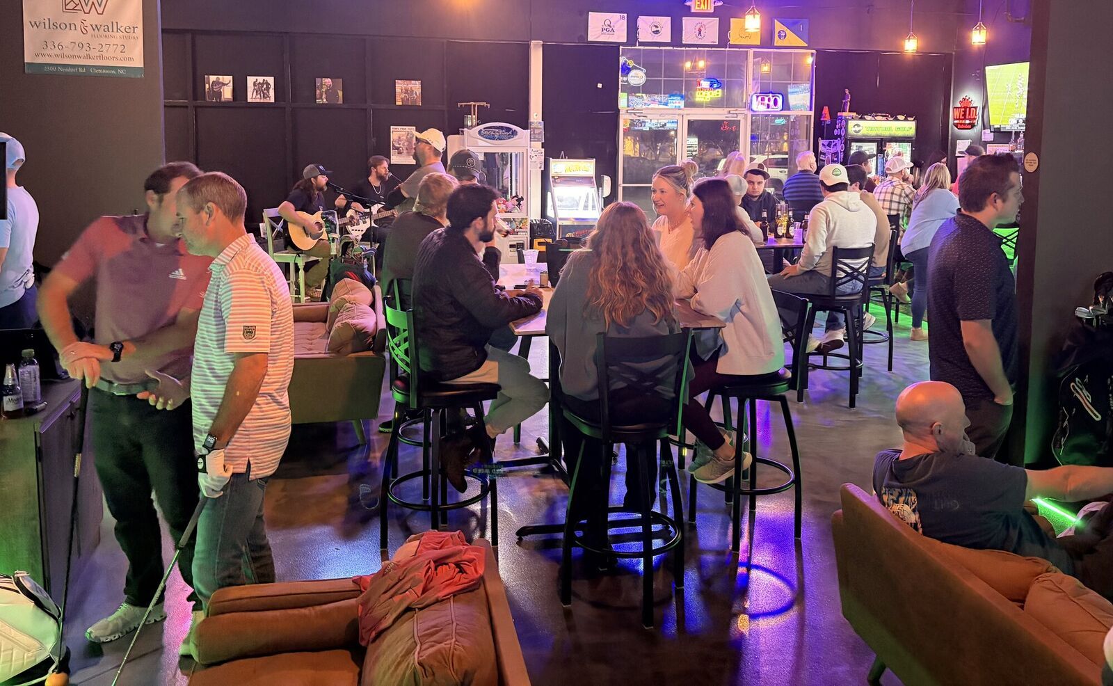 A packed night at Grip It Virtual Golf in Bermuda Run, NC: groups at the tables, a live band, and the simulator bays lit up behind them